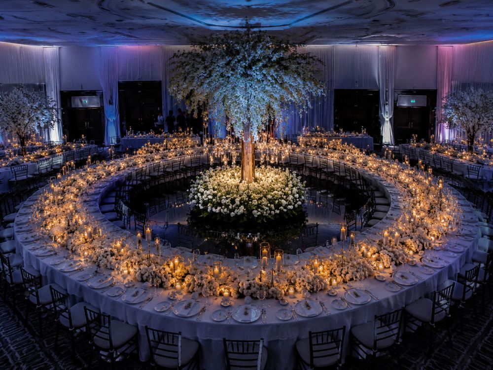 Circular curved wedding table arrangement surrounding a statement floral installation at an elegant evening reception.