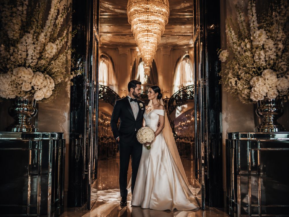 Stylish wedding couple posing in a grand ballroom doorway with modern Neo Deco architecture and luxury styling.