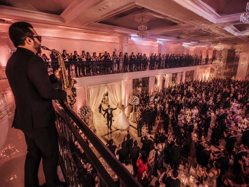 Newlyweds entering wedding reception with live saxophone performance and excited guests