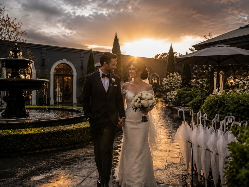 Newlywed couple walking together after rain at a Melbourne wedding venue with sunlight returning.