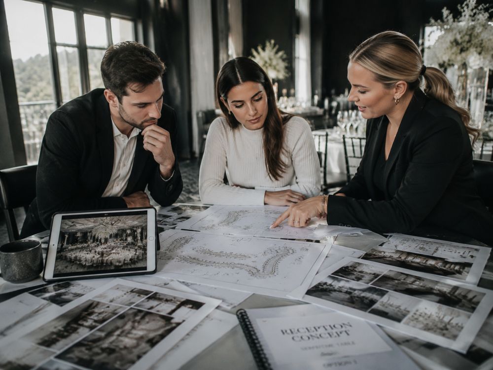 Couple and wedding stylist reviewing plans for a modern serpentine reception table design.